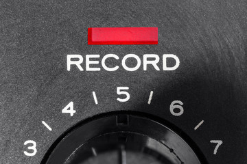 Macro close up photograph of vintage tape machine record control dial and indicator light.  