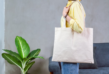 Woman in casual yellow t-shirt stand and holding bag canvas fabric for mockup logo.