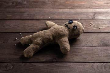 Voodoo doll on a wooden background with dramatic lighting. The concept of witchcraft and black art. Burlap doll on a wooden background. Pierce with maces. Copy space.