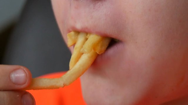 Teen boy eats french fries with sauce. Face and mouth close up view. Unhealthy fast food