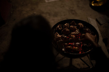 Indian Bengali woman preparing delicious kebabs on a charcoal grill on a rooftop in evening. Indian lifestyle and food. 