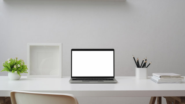 Close up of workspace with blank screen laptop, frame, stationery and tree pots on white table with white wall