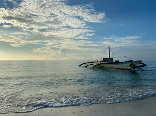 Beautiful landscape of a boat in the foreground in the sea background a blue sky with porous clouds. Calm sea with a small wave and foam. Sandy beach.