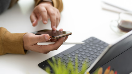 Cropped shot of  typing on smartphone while working in simple workspace with tablet and stylus