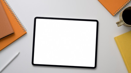 Top up view of workplace with mock up tablet, office supplies and coffee cup on white table