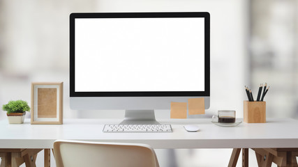 Close up view of workspace with blank screen computer, office supplies and decoration on white desk with blurred office room