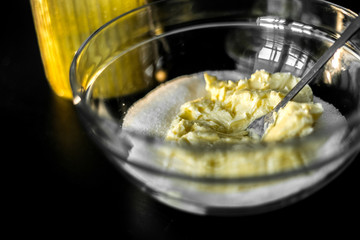 Soft butter with sugar in a glass mixing bowl with a fork. preparation of dough for cookies, cake and cakes. A black table and a jar of sugar.