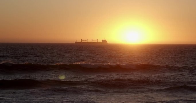 Silhouette Cargo ship moving from left to right on the ocean at sunset, Bloubergstrand, Cape town South Africa. Ocean waves at sunset with the sun just above the horizon