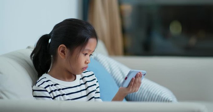 Little girl watch on mobile phone and sit on sofa at night