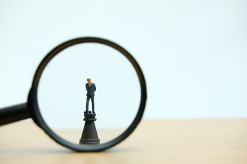 Miniature people strategic concept - magnifying a businessman standing above castle chess pawn 