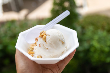 Hand holding take away cup of coconut ice cream with nature green garden background. Happy walking and eating in hot weather.