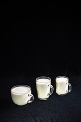 Three glass mugs with milk different in shape and volume on a background of black fabric