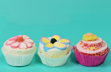 Three colorful sweet cup cakes made of foam sugar stand side by side against a green background with plenty of space for text for an invitation