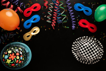Carnival objects on a black background. Coiled streamers, masks, hats, paper skeleton, confetti, paper balloons and many other carnival objects