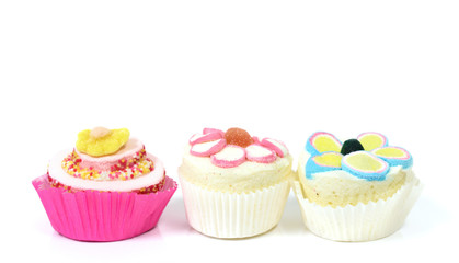 Three cute colorful cup cakes made of sugar and foam stand side by side against a white background with space for text