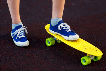 Close up legs in blue sneakers riding on yellow skateboard in motion. Active urban lifestyle of youth, training, hobby,  activity concept. Active outdoor sport for kids. Child skateboarding. 