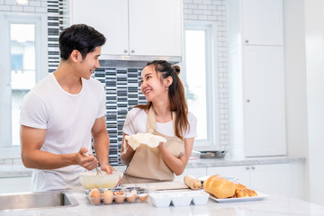 Obraz na płótnie Canvas Happy Asian couples cooking and baking cake together in kitchen room. Man and woman looking to tablet follow recipe step at home. Love and happiness concept. Sweet honeymoon and Valentine day theme