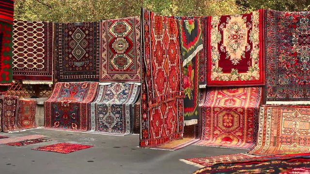 Selection of colourful rugs for sale in street in Yerevan, Armenia. slow pan right 
