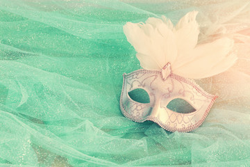 Photo of elegant and delicate white Venetian mask over mint chiffon background