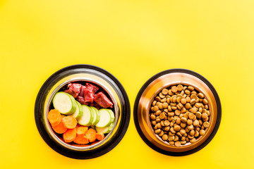 Healthy feed for cats and dogs. Bowls full of dry feed, meat and vegetables on yellow background top-down copy space