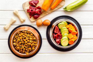 Ingredients of dry feed for dogs - meat, vegetables - near bones on white wooden background top-down