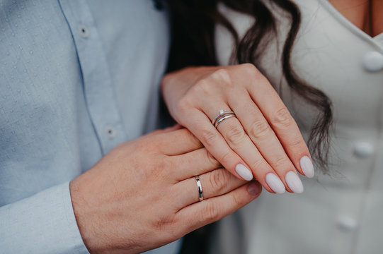 Hand On The Hand Of The Bride And Groom, Engagement Smooth Simple White Gold Rings Put On The Fingers, On The Bride’s Finger An Engagement Ring