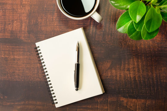 Top view of open school notebook with blank pages, Pen, Plant and Coffee cup on wooden table background. Business, office or education concept with copy space.