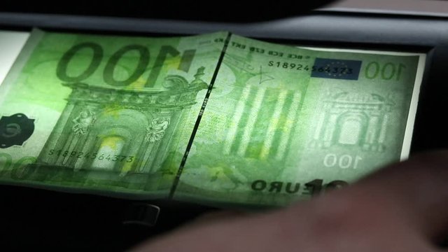 The male hand will verify the authenticity of 100 euros in ultraviolet light. Close-up