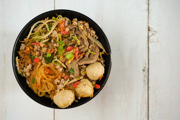 Top view noodle with minced pork , meatballs, dried shrimps and vegetables in black bowl.