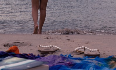woman or girl walking towards the beach with a book and an unfocused flip-flop in front