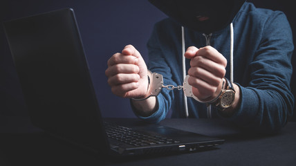 Hacker in handcuffs with laptop. Cyber crime