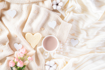 Fototapeta na wymiar Pink paper hearts with gift box and roses, coffee cup on , beige sweater on cream colour knitted blanket and fluffy background. Love and Valentine's day during Winter concept.