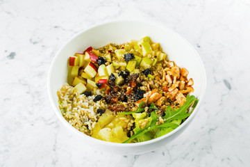 Concept of healthy food. Salad lunch bowl with mix salad, chicken breast, apple, pineapple, raising, dates, brown rice and walnut. Keto salad in bowl on marble background.
