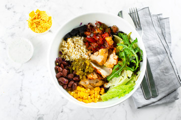 Mexican Lunch bowl on marble background. Salad bowl with corn, red beans, tomato with red onion, jalapenios, chicken breast, taco chips and yougurt garlic sauce. Top view
