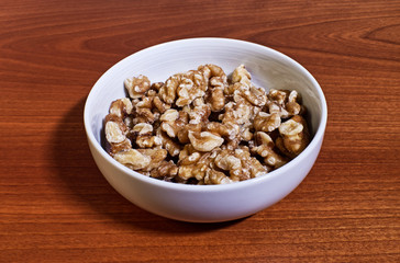 Walnuts in a white ceramic bowl on wooden table