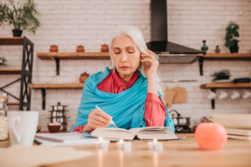 Grey-haired beautiful elderly lady in blue shawl making notes