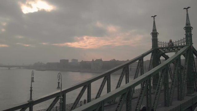 aerial flying forward drone shot above the Liberty Bridge in Budapest towards a university at the riverside on a cloudy winter day