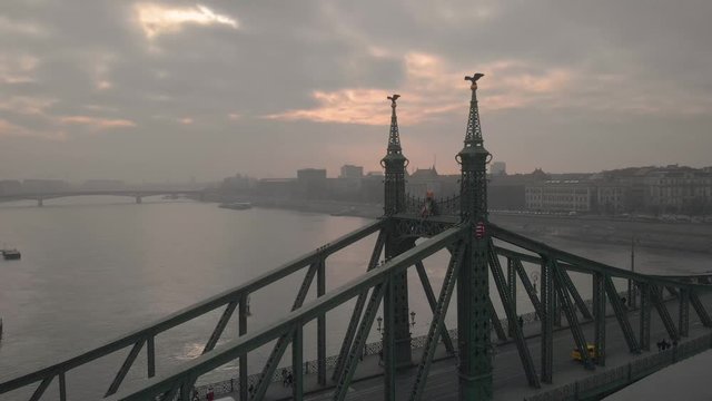 aerial rotating drone shot around the Liberty Bridge in Budapest with a university building and the river in the background on a cloudy winter day