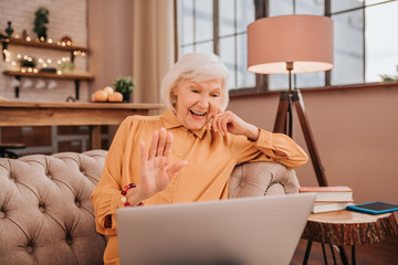Grey-haired beautiful lady in orange blouse greeting her friend online