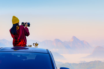 Woman traveller photographer sitting to takes a photo shot on her owns roof of the car with scenery...