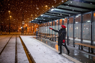 woman looking at snow standing at tram station winter night