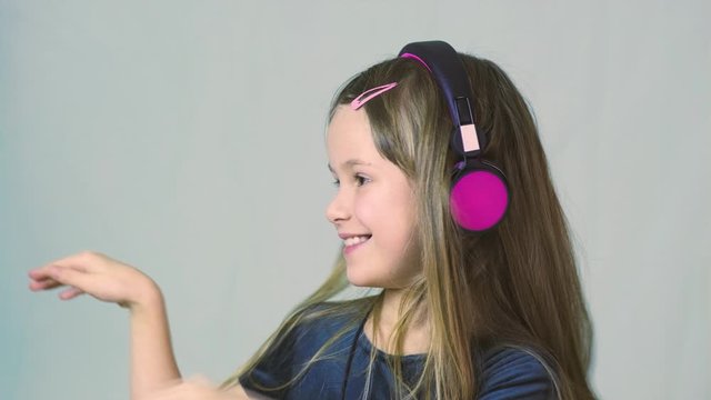 Pretty smiling cild girl listening to music in big pink earphones.