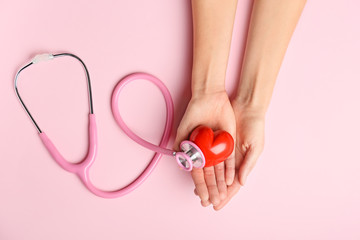 Female hands with red heart and stethoscope on color background. Cardiology concept
