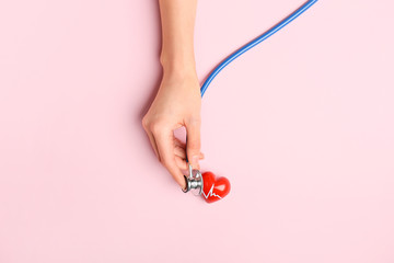 Female hand with red heart and stethoscope on color background. Cardiology concept