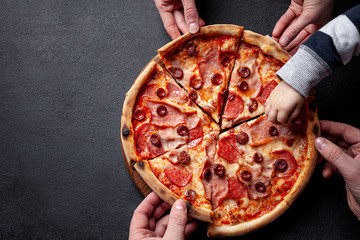 Italian Cuisine. Pepperoni pizza with salami sausage and red hot pepper, lies on a wooden board, on a black background. background image, copy space text