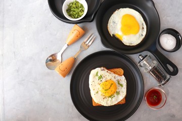 Fried Egg on Whole wheat Toast with salt and pepper for classic Breakfast. sunny side up egg with brown bread on black plate over wooden table, top view, copy space.