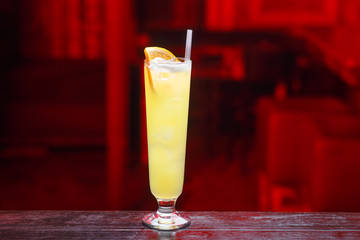 Closeup of a long glass of orange juice with gin, which sits on the bar counter, isolated on a red light background. Horizontal view.