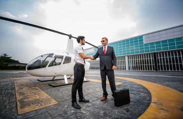 Commercial pilot in uniform greeting clients near small private helicopter on a landing point