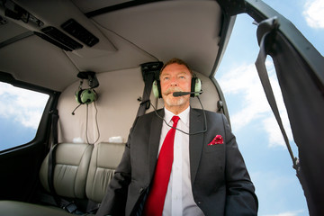 Calm concentrated business executive man or CEO talking the microphone of his headphones while sitting in the helicopter cabin
