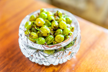 Closeup of many ripe green gooseberries berries healthy sour fruit in crystal glass dish bowl on...
